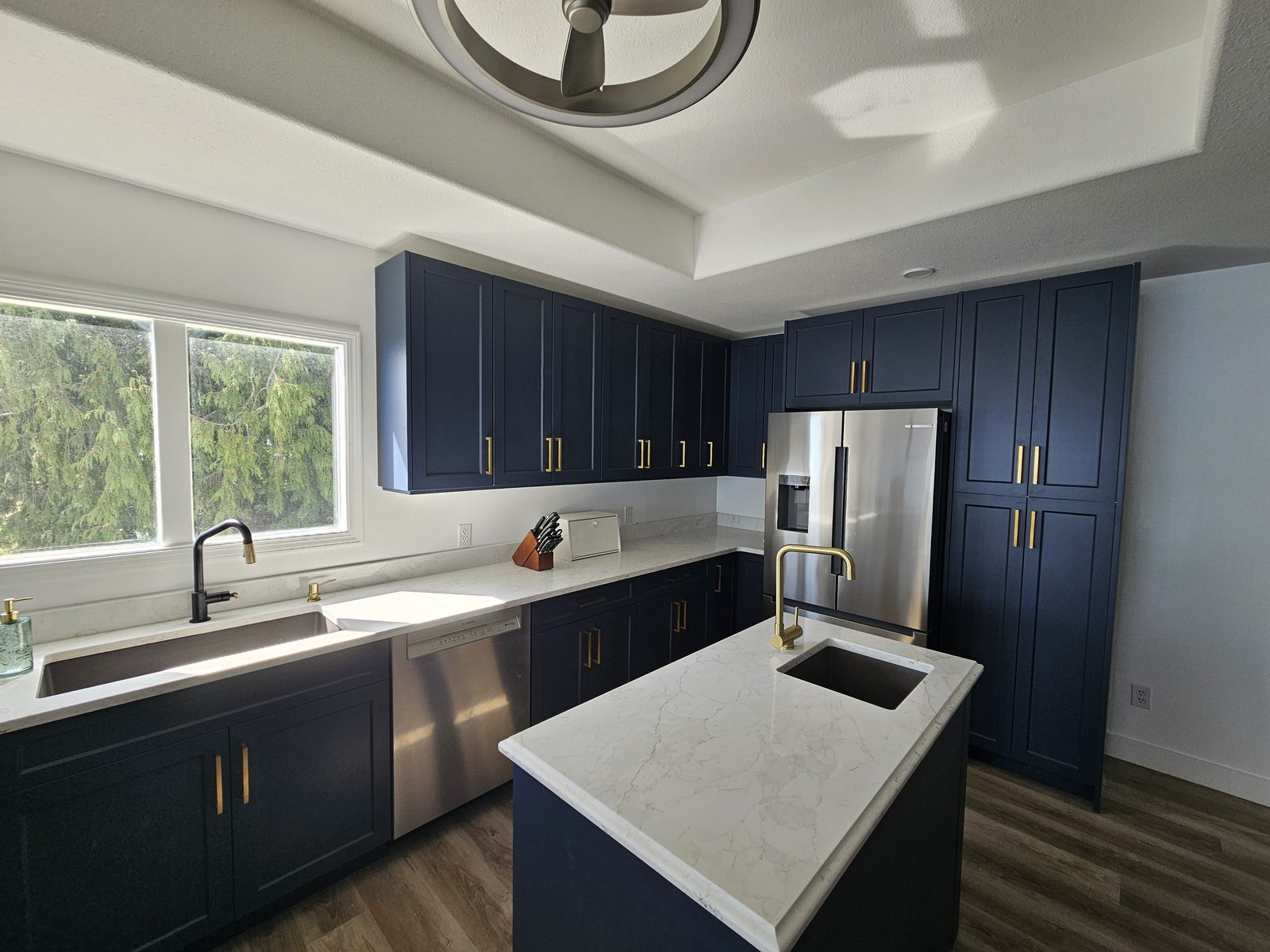 A renovated kitchen with navy cabinets, quartz counters and an island sink